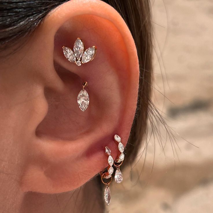 a close up of a person's ear with three diamond earrings