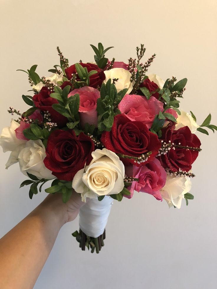 a bouquet of red, white and pink flowers in someone's hand on a white background