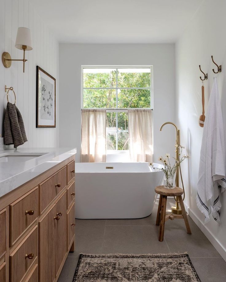 a white bath tub sitting under a window next to a wooden cabinet and counter top