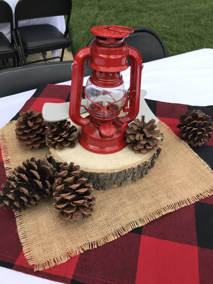 a red lantern sitting on top of a table next to two pinecones and a burlap placemat