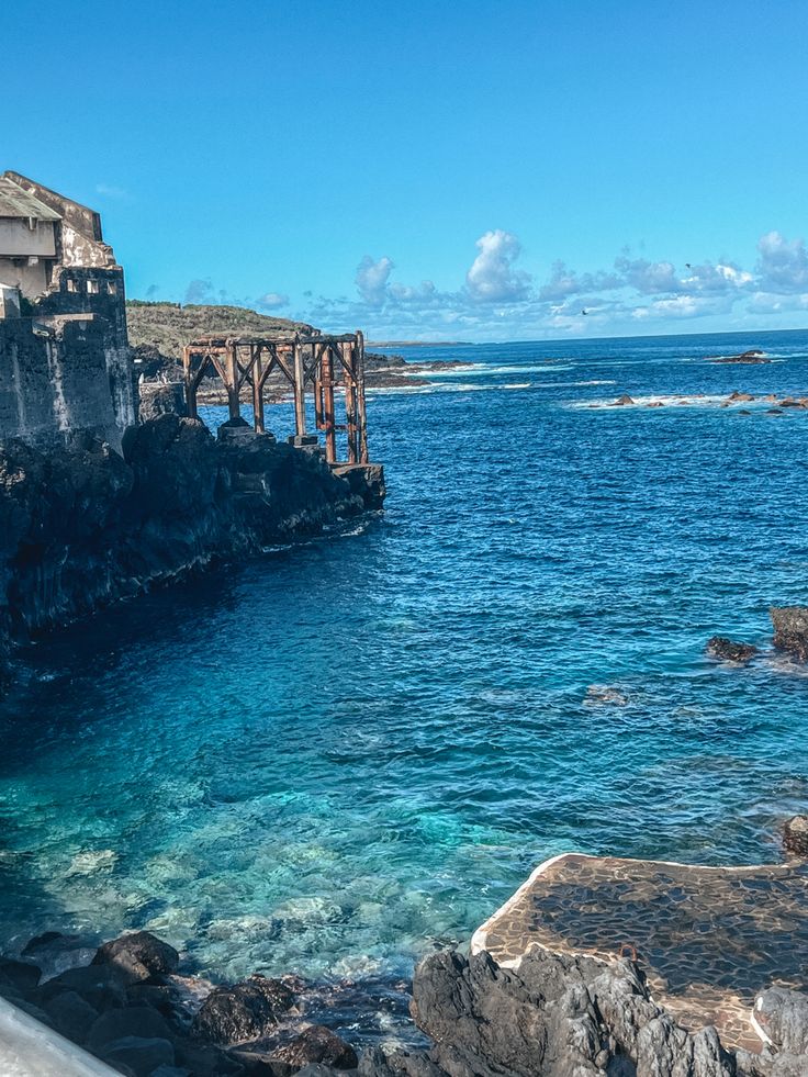 the ocean is clear and blue with rocks on both sides as well as an old bridge