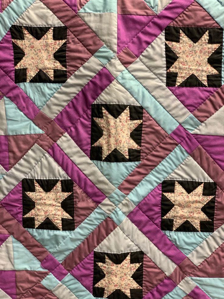 a close up of a quilt with stars on the top and purple, black, and white squares