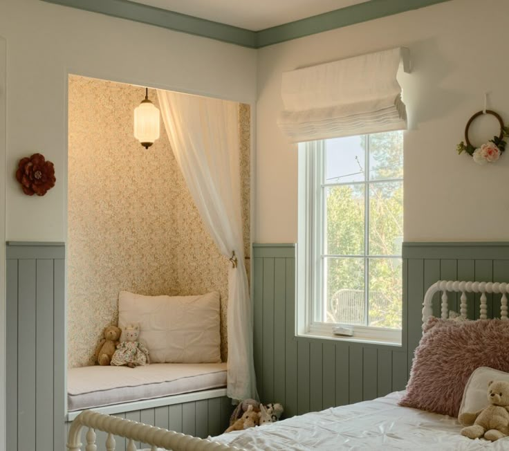 a white bed sitting in a bedroom next to a window filled with pillows and stuffed animals