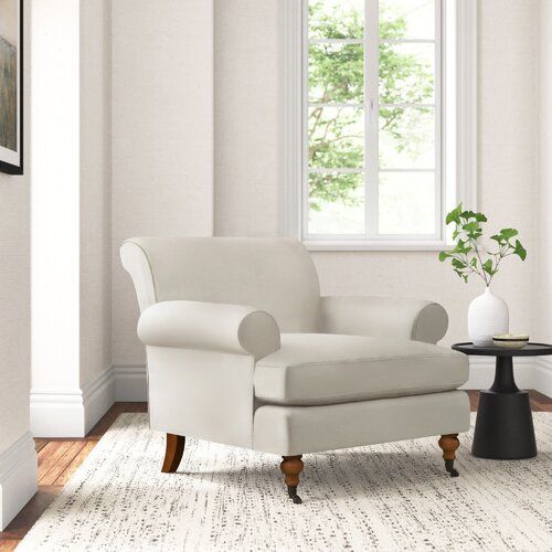 a white chair sitting in front of a window next to a table with a vase on it