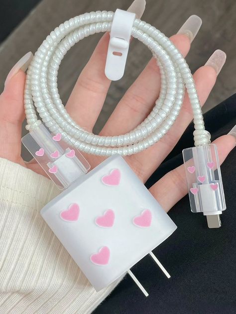 a hand holding a white and pink cable with hearts on it, next to a cell phone charger