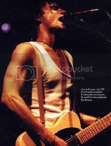 a man holding a guitar in front of a microphone and an advertisement for the band