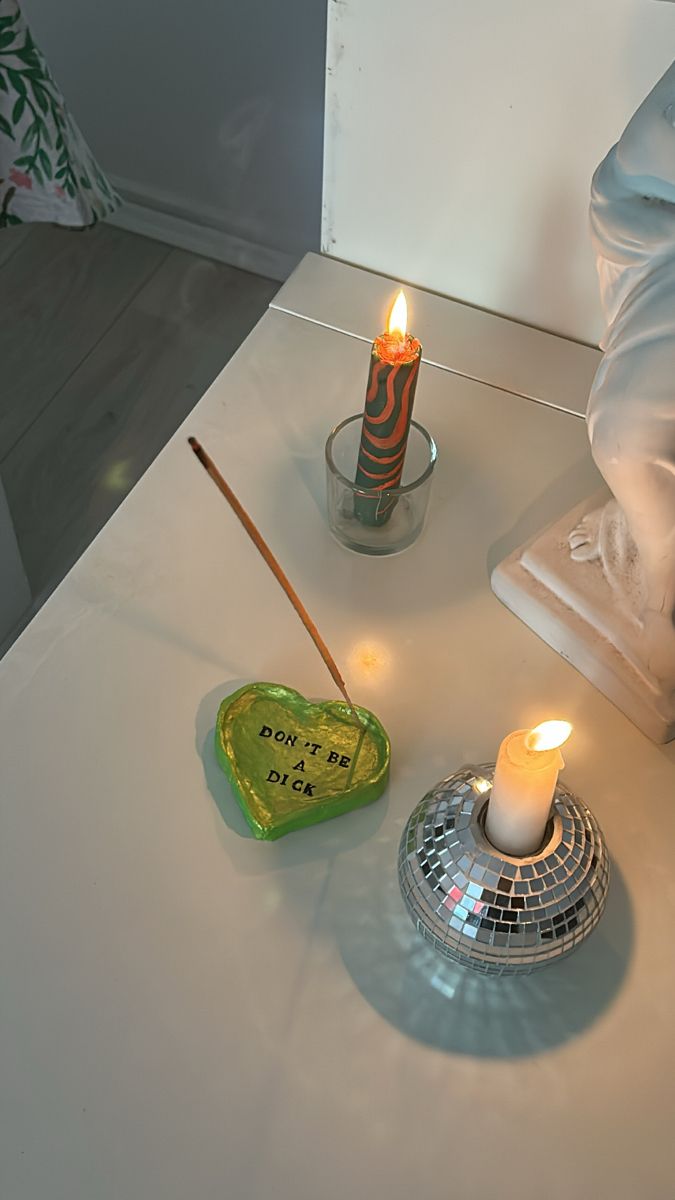 two lit candles sitting on top of a white table next to a heart shaped bowl