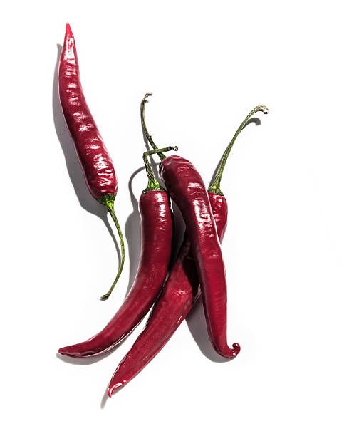 three red chili peppers on a white background with one pepper still attached to the other