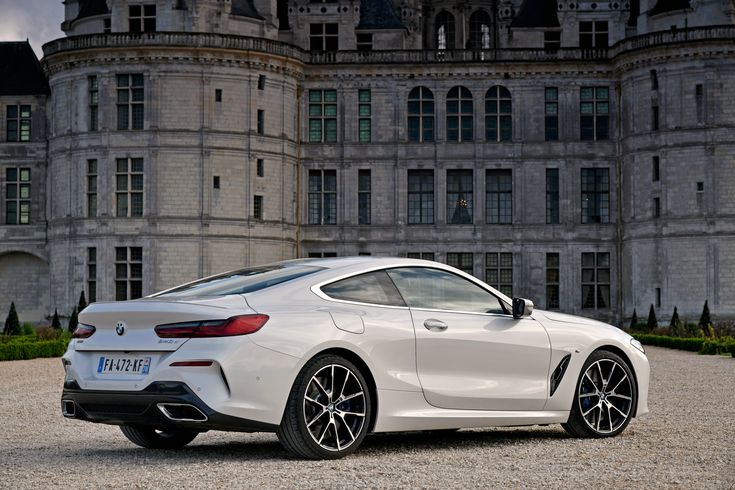 a white sports car parked in front of a large building with an old castle behind it