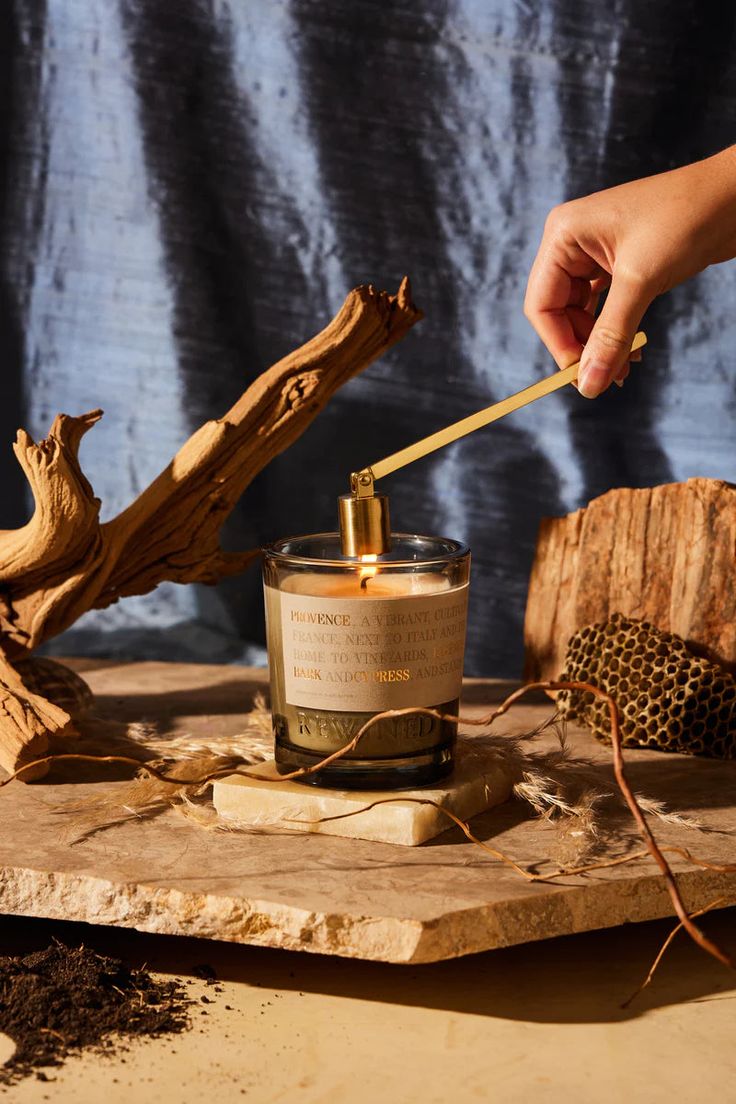 a person holding a wooden spoon over a jar on top of a piece of wood