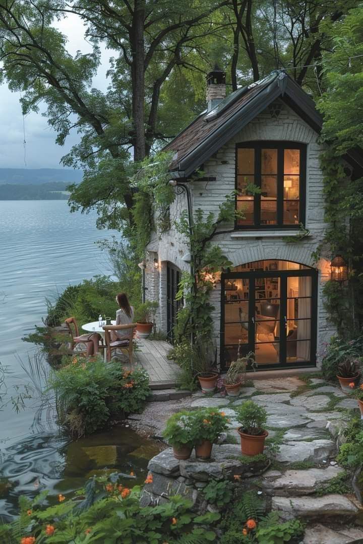 a small house sitting on top of a lake next to a lush green forest covered hillside