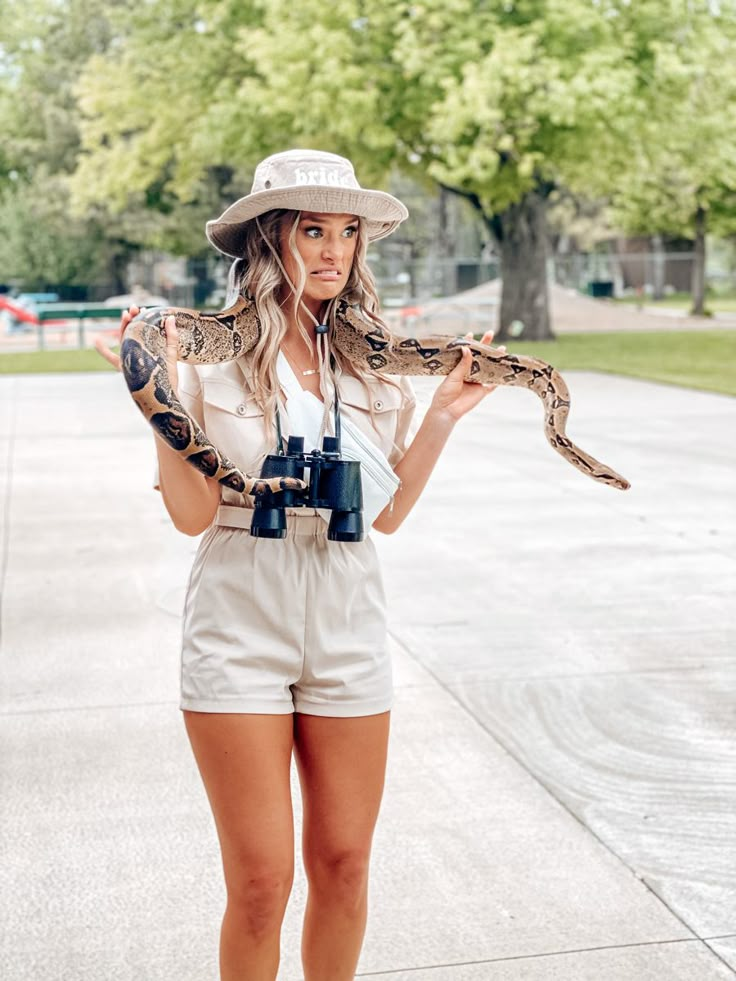 a woman in white shorts and hat holding a snake around her neck while wearing a camera