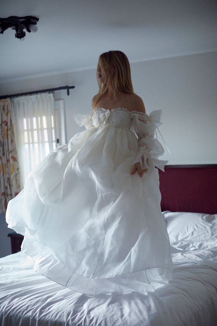 a woman in a white dress standing on top of a bed