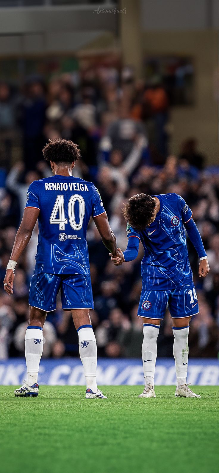 two soccer players in blue uniforms standing on the field with their hands together, facing each other