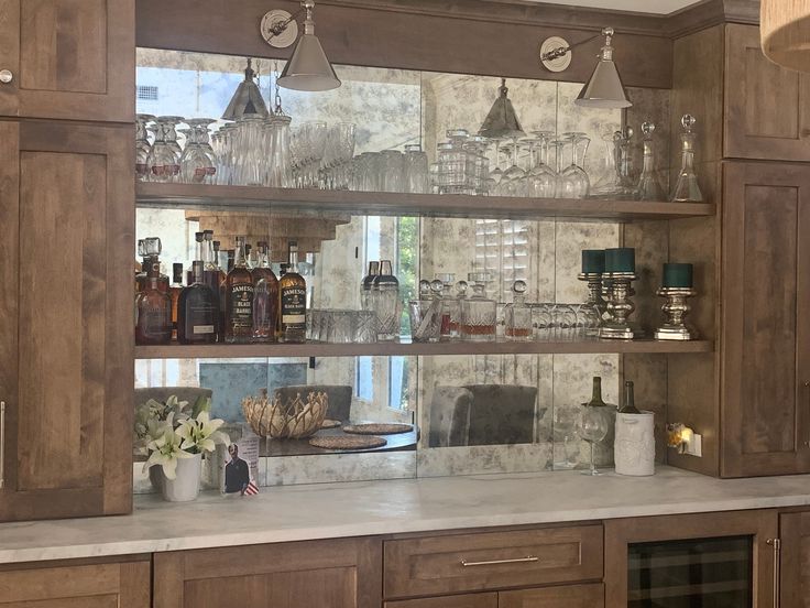 a kitchen with wooden cabinets and shelves filled with glasses, liquor bottles and vases