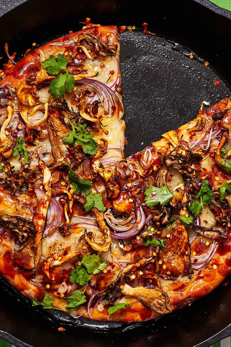 a pizza with onions, mushrooms and herbs in a black pan on a green tablecloth