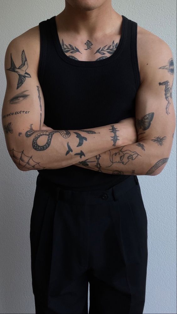 a man with tattoos on his arms and chest standing in front of a white wall