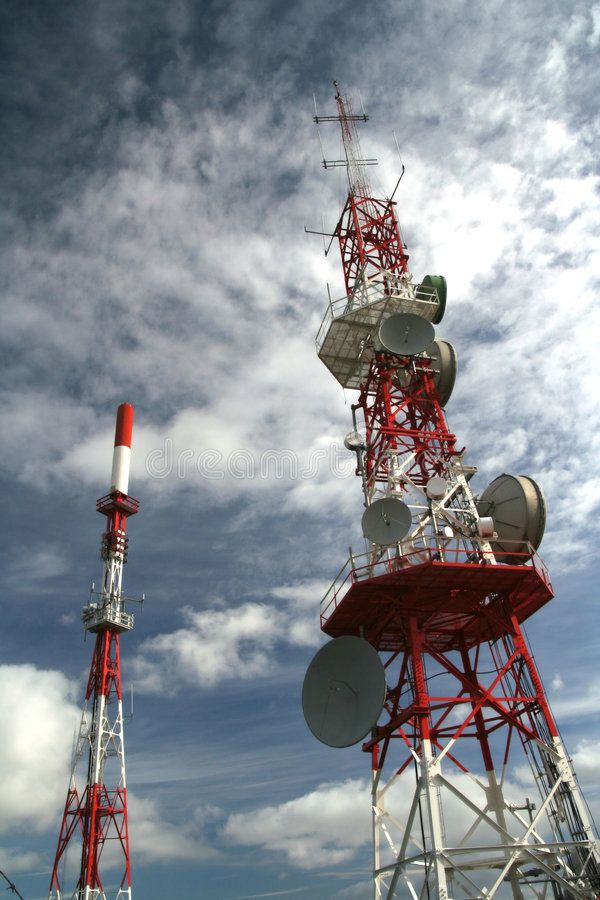 two red and white radio towers against a cloudy blue sky