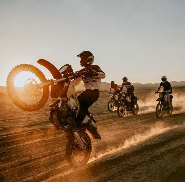 several people riding dirt bikes on a dusty road at sunset with the sun behind them