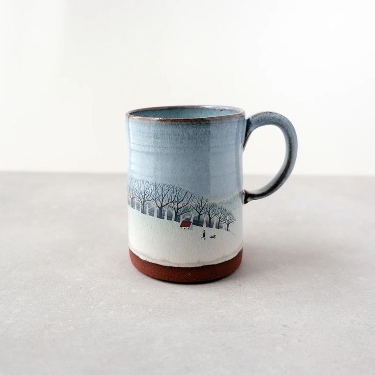 a blue and white coffee mug with trees on the side, sitting on a table