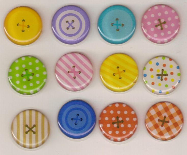 six different colored buttons are arranged in a row on a white surface with polka dots and crosses