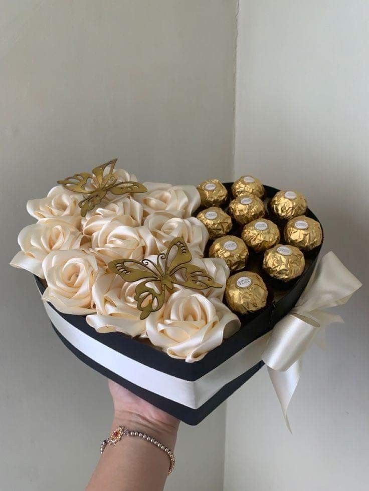 a hand holding a heart shaped box filled with chocolate covered roses and gold foils