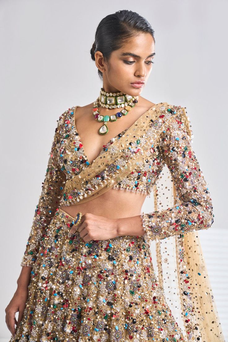 This antique gold net lehenga set has a dense sprinkling of all jewel tones of embroidery material - emerald, ruby, turquoise, gold, silver, pearl etc. It comes with a full sleeves blouse which has delicate tasselling at the sleeve hem and at the waist. The dupatta has four-sided border and dense sprinkling.From Seema Gujral’s Samode collectionDELIVERY TIMEPlease wait 8-12 weeks for your outfit to arrive.FABRIC DETAILSNetProfessional cleaning only. Elegant Pre-draped Kundan Saree For Party, Festive Gold Embellished Pre-draped Saree, Gold Pre-draped Saree For Reception, Multicolor Long Sleeve Traditional Wear With Sheer Dupatta, Festive Embellished Pre-draped Saree With Long Sleeves, Festive Embellished Long Sleeve Pre-draped Saree, Festive Long Sleeve Embellished Pre-draped Saree, Multicolor Blouse Piece With Sheer Dupatta For Reception, Festive Kundan Lehenga