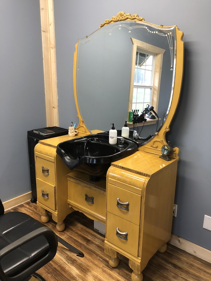 a yellow vanity with a black sink and mirror in a room next to a chair