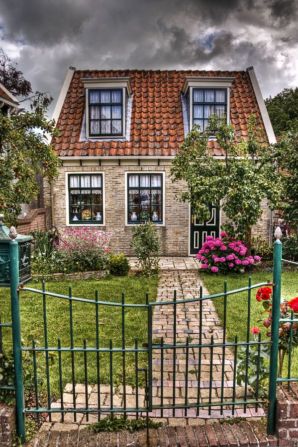 a house that is next to a fence and some flowers in front of the house