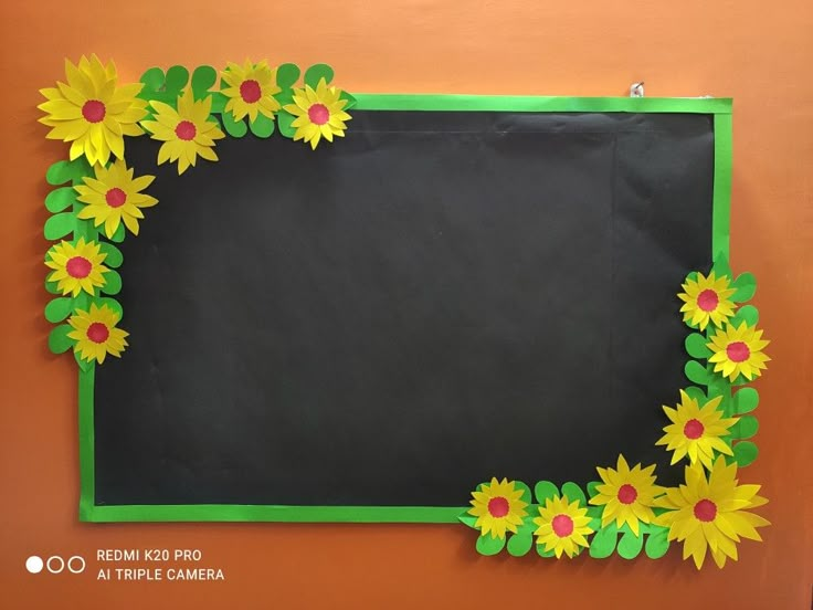 a blackboard with yellow and red flowers on it is mounted to an orange wall