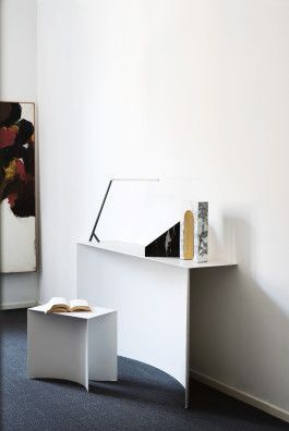 a room with a white desk and black carpeted floor next to a painting on the wall