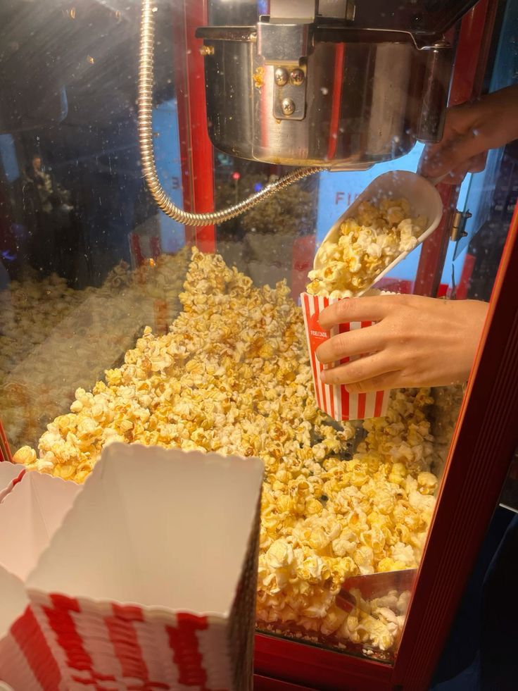 popcorn being poured into a red and white box in front of a large machine that is filled with it