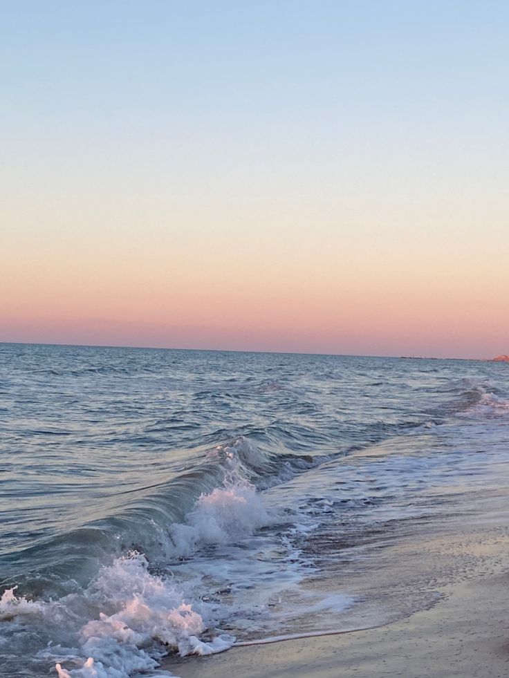 an ocean beach with waves coming in to shore and the sun setting on the horizon