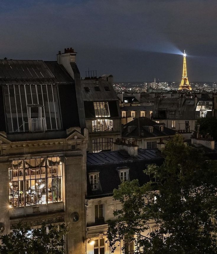 the eiffel tower is lit up in the distance from some buildings at night