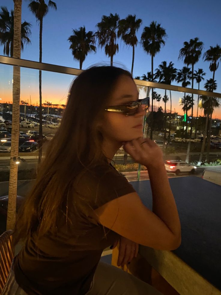 a woman sitting at a table with her hand on her chin looking out the window