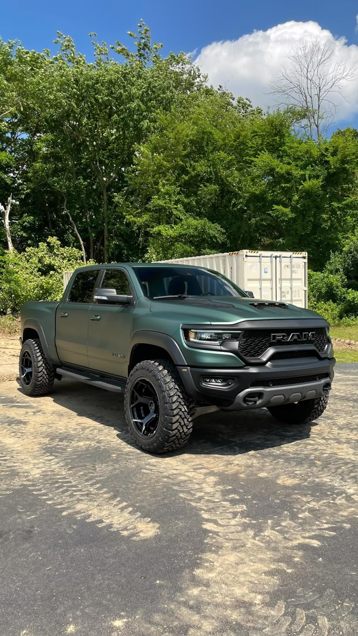 a green truck parked on top of a parking lot next to some trees and bushes