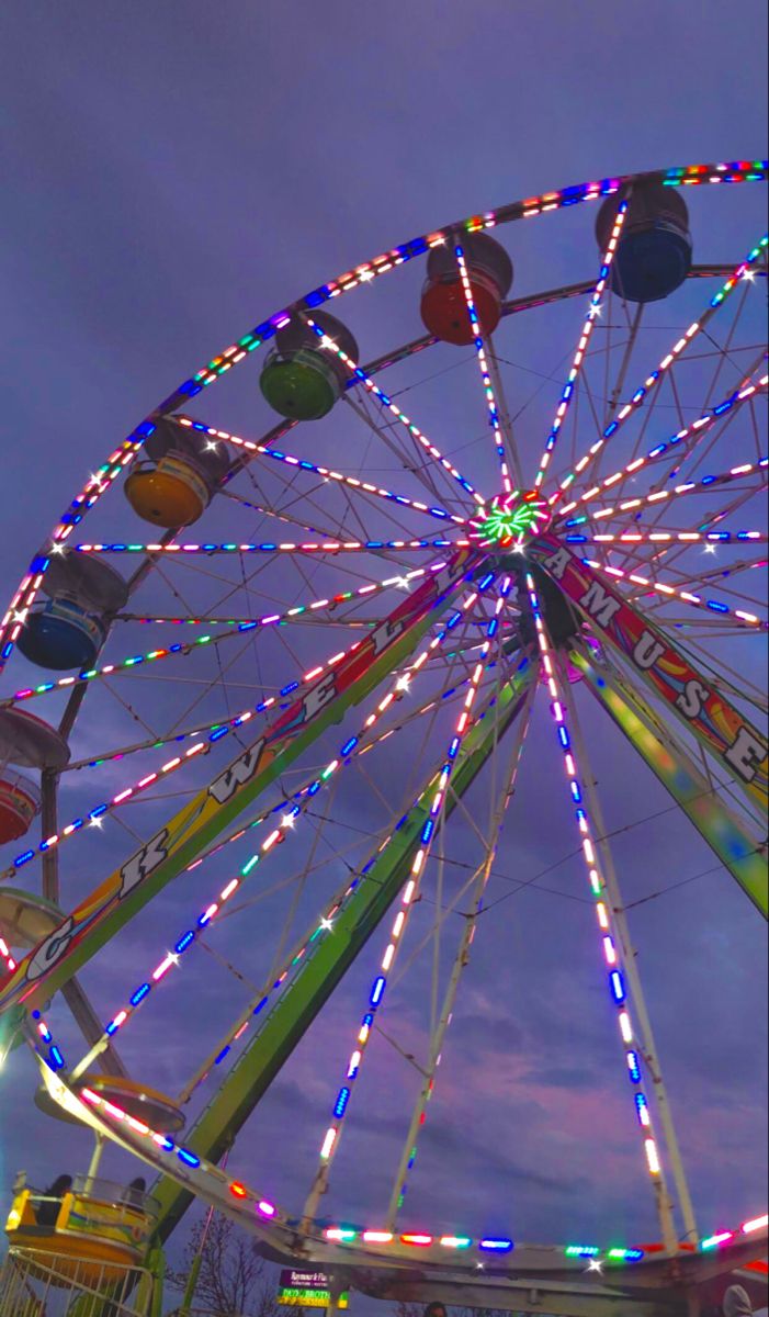 a ferris wheel lit up at night with colorful lights on it's sides and the sky in the background