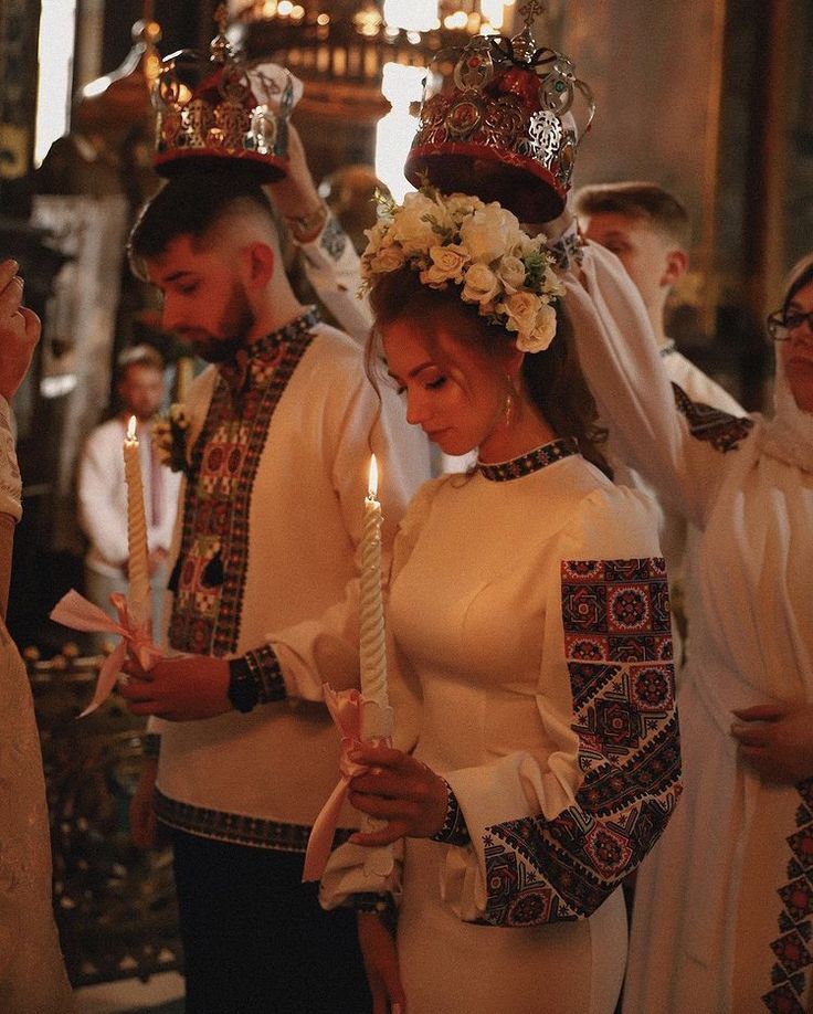 two people wearing crowns and holding candles in front of other people at a wedding ceremony