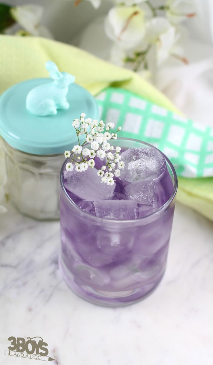 a glass filled with ice and flowers on top of a marble table next to a jar