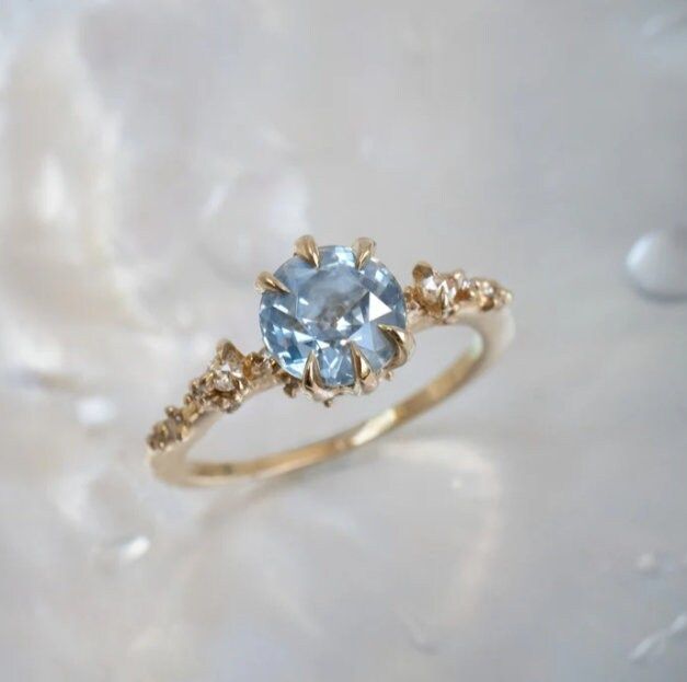 a gold ring with an aqua blue topazte surrounded by small diamond accents on a white background