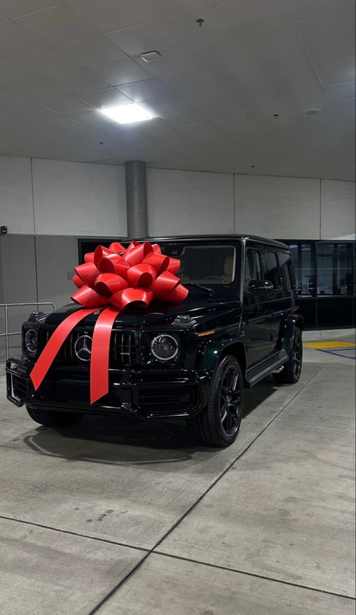 a black car with a red bow on the hood is parked in a parking garage