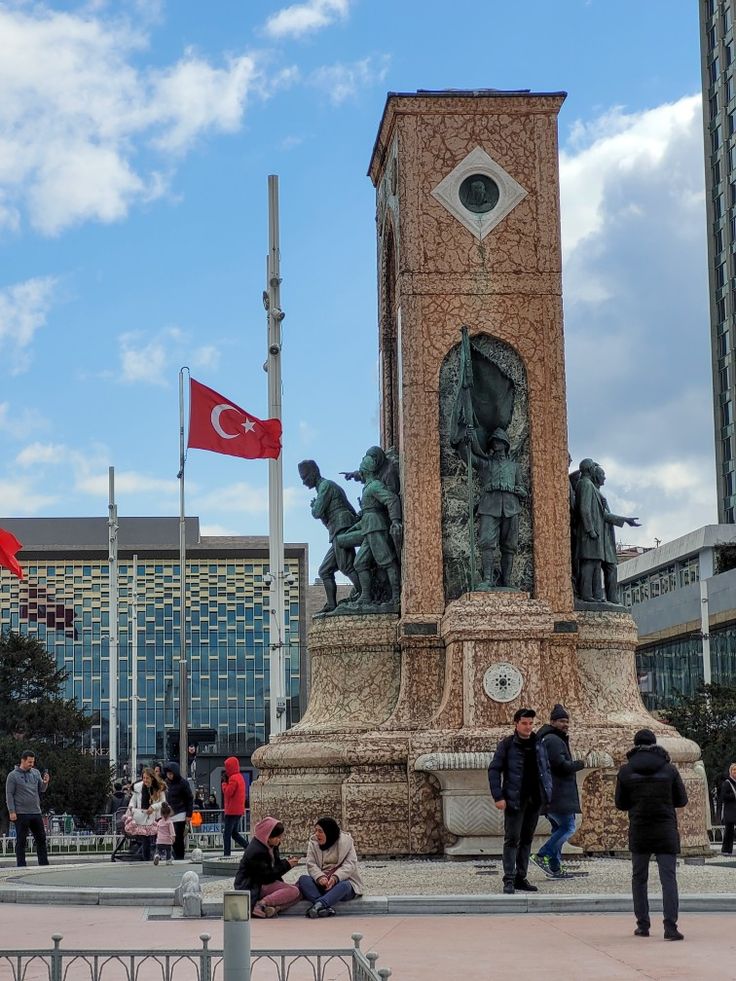 people are sitting on the ground in front of a monument with a flag flying above it