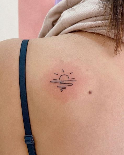 the back of a woman's shoulder with a small sun tattoo on her left side