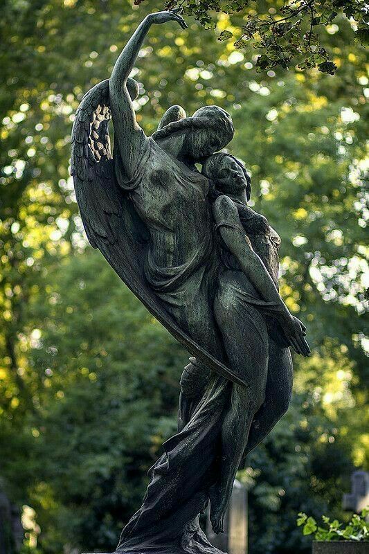 a statue with an angel holding a child in it's arms, surrounded by trees