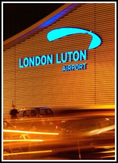 the london luton airport sign lit up at night with cars passing by in front