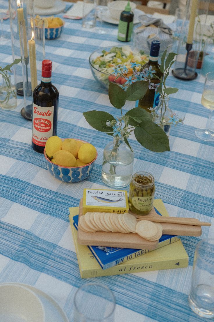 a blue and white checkered table cloth with food on it, candles, plates and glasses