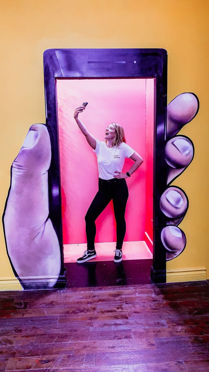 a woman standing in front of a pink and purple wall with her hands up to the side