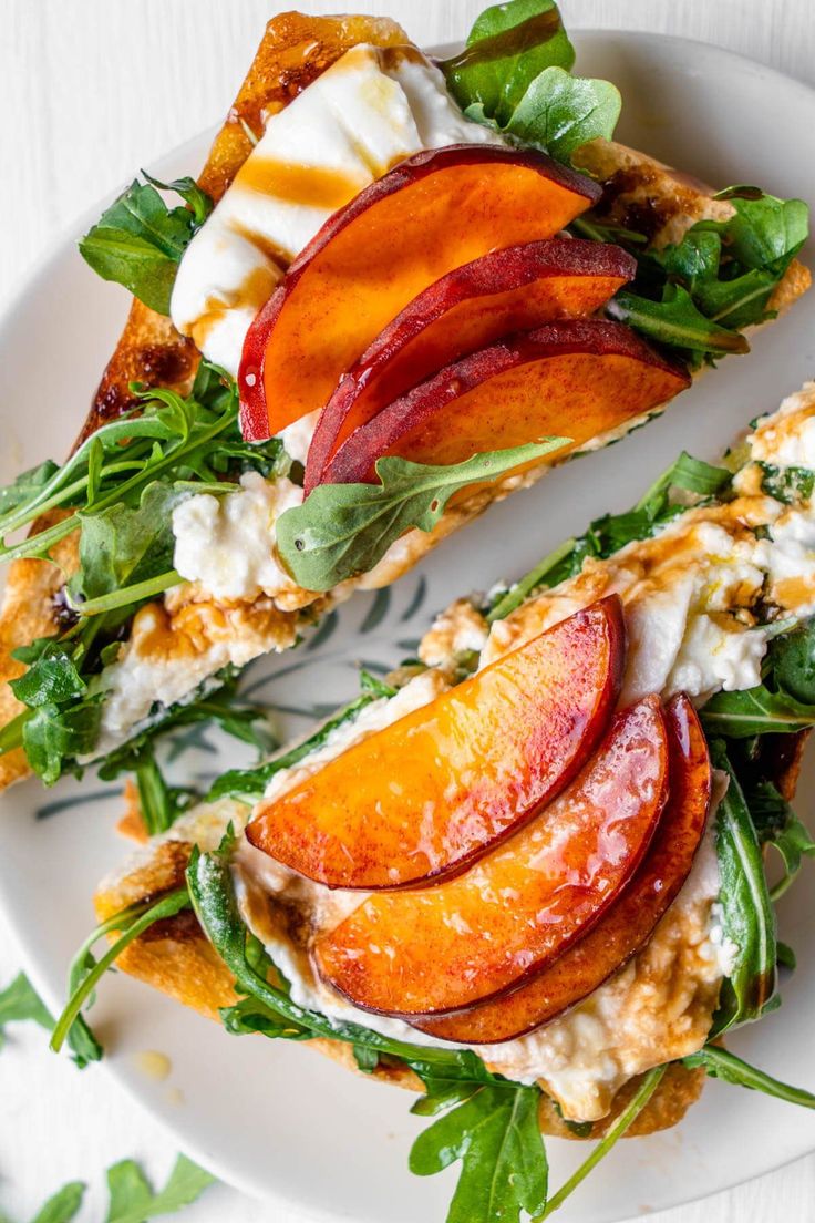 two slices of peach and goat cheese sandwich on a white plate with green leafy greens