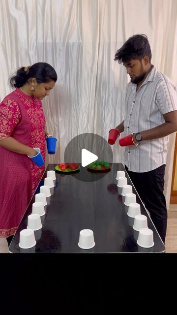 a man and woman standing in front of a black table with cups on top of it