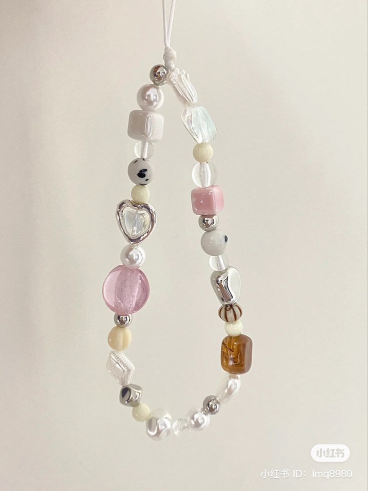 a beaded necklace hanging on a white wall with beads and charms attached to it